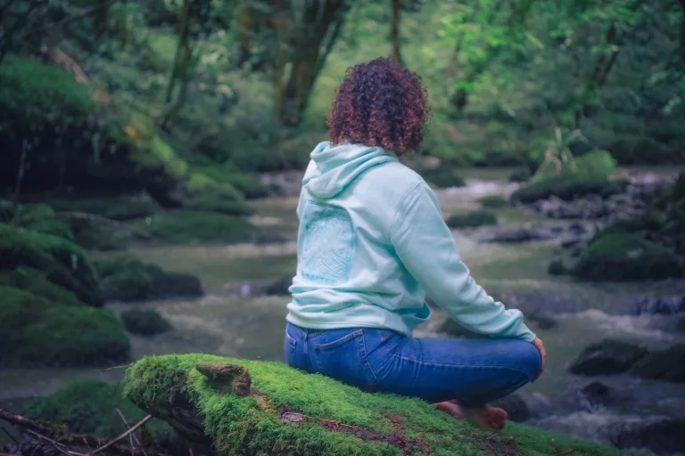 Photo d'une femme en tailleur sur un rocher moussu en pleine méditation portant le sweat de l'eau de la nouvelle collection de Lunélys Création