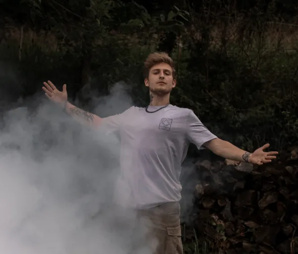 Un homme debout, les bras ouverts, portant le t-shirt “AIR” de la collection de Lunélys, avec une brume légère autour de lui. Le logo côté cœur symbolise le concept artistique de l’air.