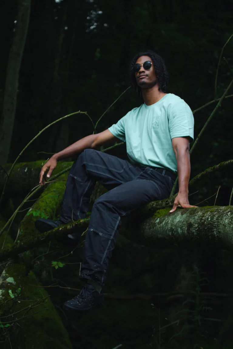 Photo d'un homme portant une paire de lunette de soleil de profil assis sur une branche, il porte le t-shirt de la Terre de la nouvelle collection de Lunélys Création