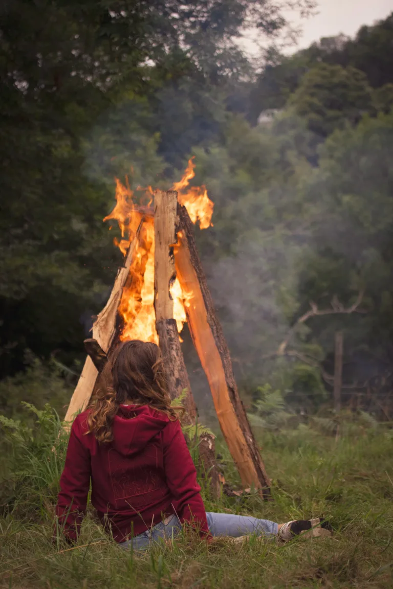 Photo d'une femme de dos devant un feu de camp assise et contemplative