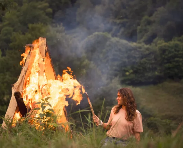 T-shirt beige avec un motif subtil, porté par une femme dans un cadre naturel près d’un feu de camp entouré de bûches.
