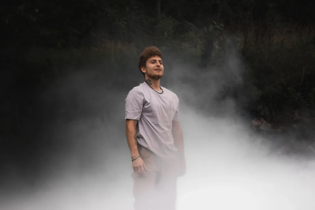 Un homme debout dans une brume légère, portant le t-shirt “AIR” de la collection de l’artiste Lunélys, avec un logo côté cœur représentant le concept de l’air.