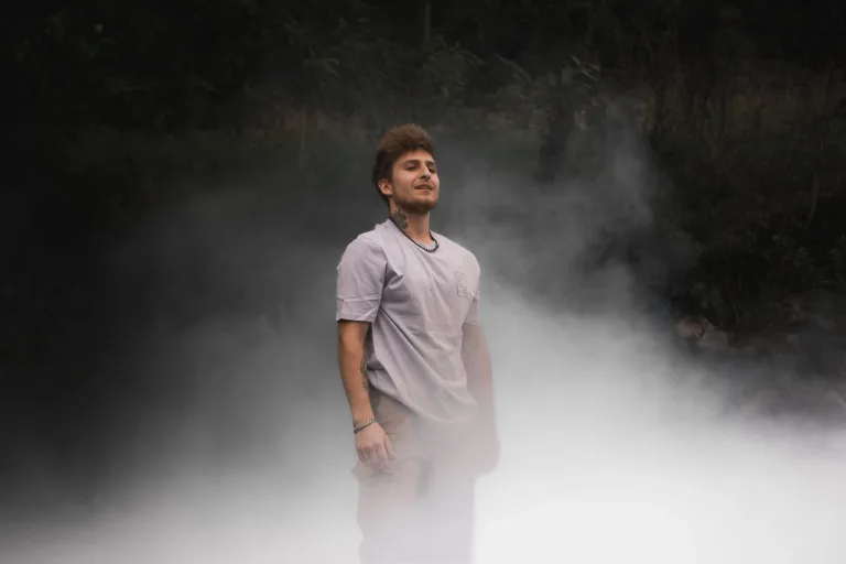 Un homme debout dans une brume légère, portant le t-shirt “AIR” de la collection de l’artiste Lunélys, avec un logo côté cœur représentant le concept de l’air.