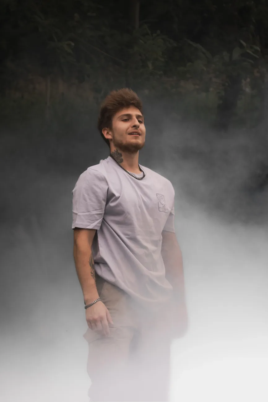 Un homme debout dans une brume légère, portant le t-shirt “AIR” de la collection de l’artiste Lunélys, avec un logo côté cœur représentant le concept de l’air.