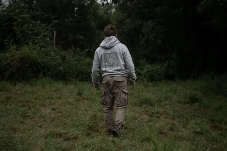 sweat-air-brode-lunelys-marche-nature Un homme marchant dans une prairie, vu de dos, portant le sweat-shirt gris “AIR” de la collection Lunélys, avec un design brodé artistique sur le dos.